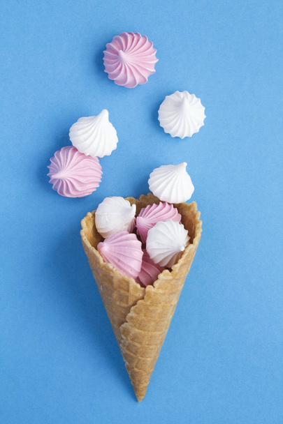 Ice cream cone with pink and white meringue  in the center of the blue background. Top view. Copy space. Location vertical. - Photo, Image