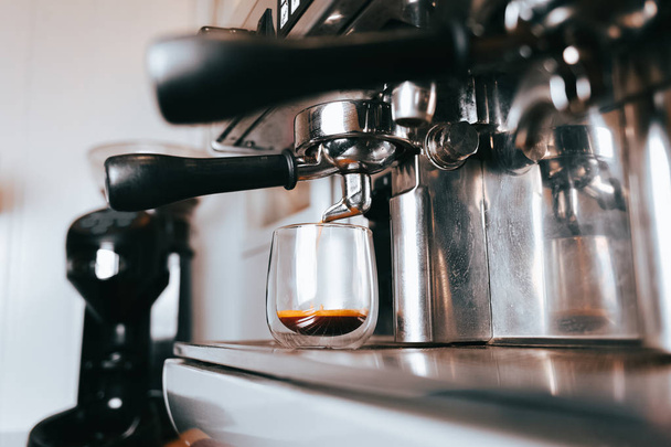 Ароматный эспрессо течет из кофеварки в чашку. Изготовление ароматного кофе с профессиональным кофейным оборудованием
 - Фото, изображение
