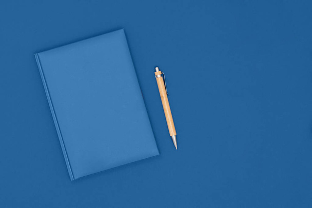 ノートと青の背景にペン。ビジネスコンセプト。トップビュー、フラットレイアウト、コピースペース。2020年の流行色. - 写真・画像