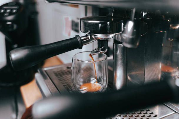 Aus einer Kaffeemaschine strömt duftender Espresso in eine Tasse. Zubereitung von aromatischem Kaffee mit professioneller Kaffeeausrüstung - Foto, Bild