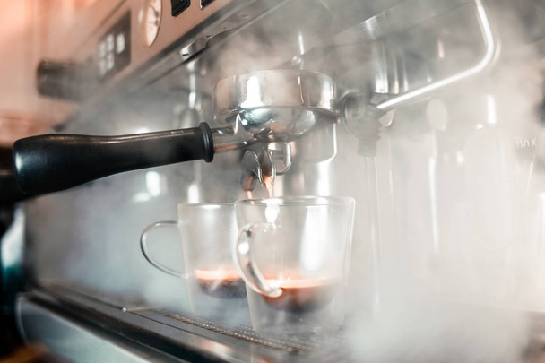 Az illatos eszpresszó a kávéfőzőből egy pohárba folyik. Illatos kávé készítése professzionális kávéfőző berendezéssel - Fotó, kép