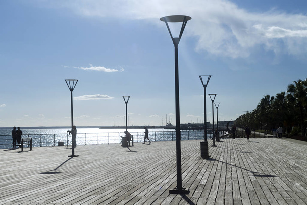 Limassol, Cyprus, December 27th, 2019: Wooden pier on the Molos promenade with street lamps and a few people on a sunny winter day - Фото, изображение
