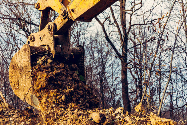 Екскаватор виконує розкопки, викопуючи землю відром у лісі
. - Фото, зображення