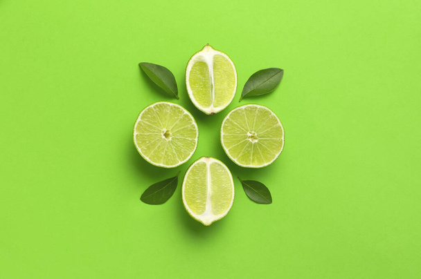 Fresh juicy lime and green leaves on bright green background. Top view flat lay copy space. Creative food background, tropical fruit, vitamin C, citrus. Composition with whole and slices of lime - Photo, Image