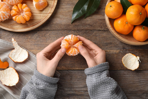 Woman holding peeled ripe tangerine at wooden table, top view - Foto, Imagem