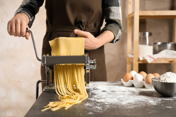 Nainen valmistelee nuudeleita pastakoneella pöydässä sisätiloissa
 - Valokuva, kuva