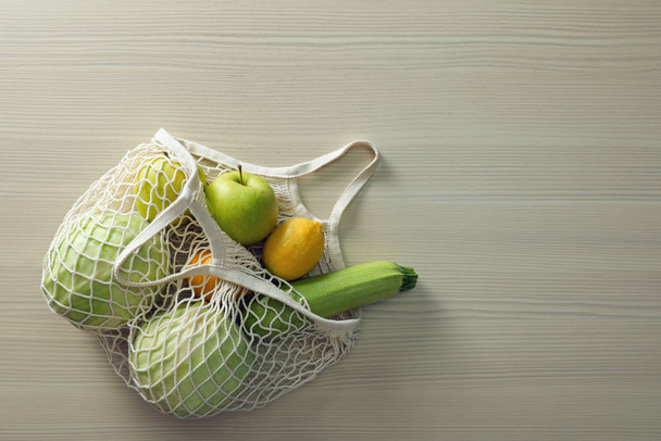 Net bag with vegetables and fruits on wooden table, top view. Sp - Foto, immagini
