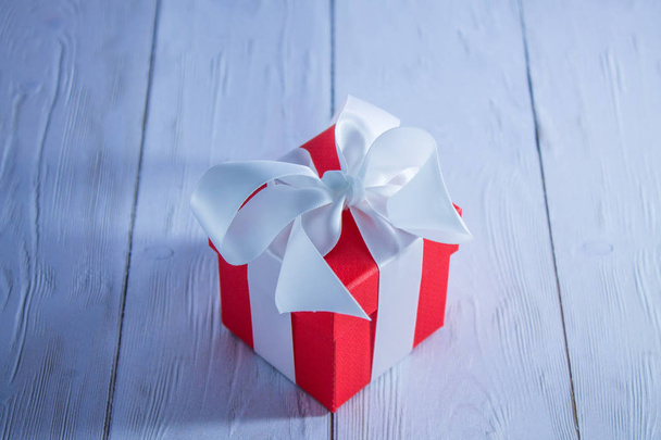 Red square gift box with satin bow on white table - 写真・画像