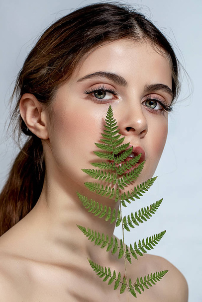 Portrait of an adult brunette woman on a white background with green fern - Photo, image