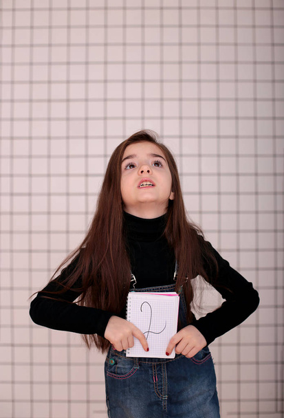 молода усміхнена дівчина восьми років з довгим волоссям в чорному черепаховому і джинсовому сарафанах зі знаком "2 два
" - Фото, зображення