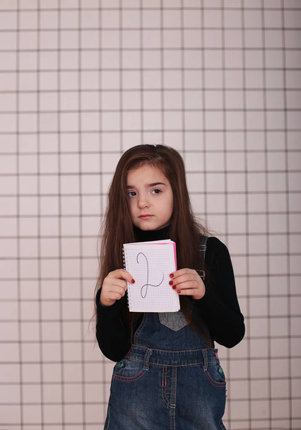 nuori hymyilevä tyttö kahdeksan vuotta pitkät hiukset musta poolopaita ja denim sundress kanssa merkki "2 kaksi
" - Valokuva, kuva