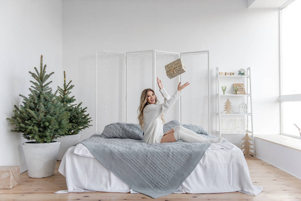 A sweet and beautiful girl in a white sweater and leggings is basking in her big bed - Fotografie, Obrázek