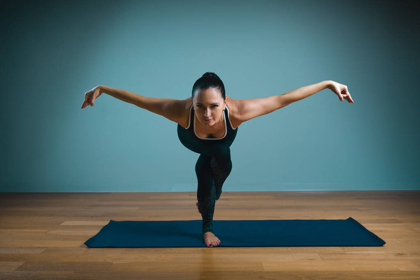 Спортивная молодая женщина делает растяжку. Стройная девушка практикует йогу в помещении на синем фоне. Спокойствие, отдых, концепция здорового образа жизни
. - Фото, изображение