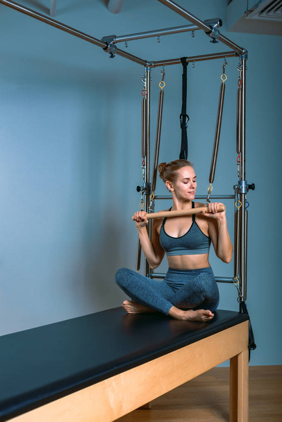 Young girl doing pilates exercises with a reformer bed. Beautiful slim fitness trainer on reformer gray background, low key, art light. Fitness concept - Foto, Imagen
