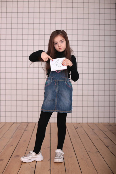 joven chica enojada de ocho años con el pelo largo en un cuello alto negro y vestido de mezclilla con el signo "NO
" - Foto, imagen