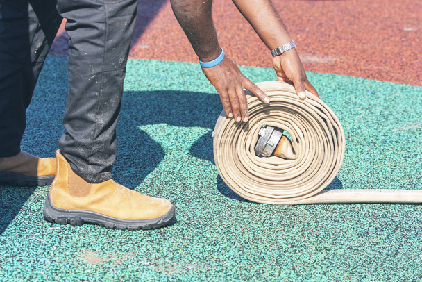 Limpiador enrollando la manguera en el campo de deportes
 - Foto, Imagen
