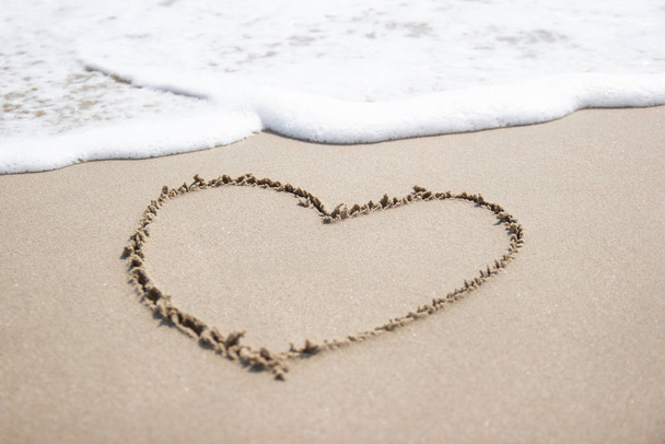 Herz-Symbol auf einem Sand am Strand mit sanfter Welle zum Hintergrund - Foto, Bild