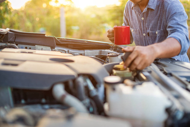 Asian man holding a red coffee cup and checking the engine of hi - Foto, Imagem