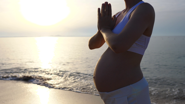 Νεαρή έγκυος γυναίκα κάνει γιόγκα στην παραλία με τα χέρια σε Namaste αίσθημα ευγνωμοσύνης. - Πλάνα, βίντεο