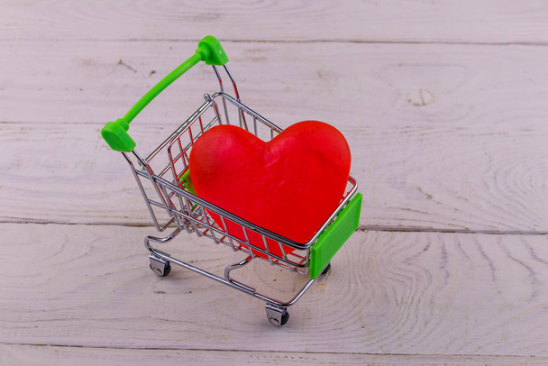 Shopping cart with big red heart on white wooden background. Valentines Day concept - Valokuva, kuva