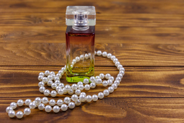 Bouteille de parfum et collier de perles sur fond bois
 - Photo, image