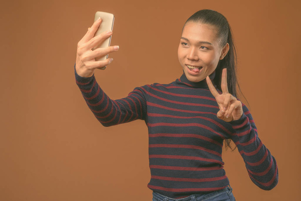 Nuori kaunis aasialainen transsukupuolinen nainen ruskeaa taustaa vasten
 - Valokuva, kuva