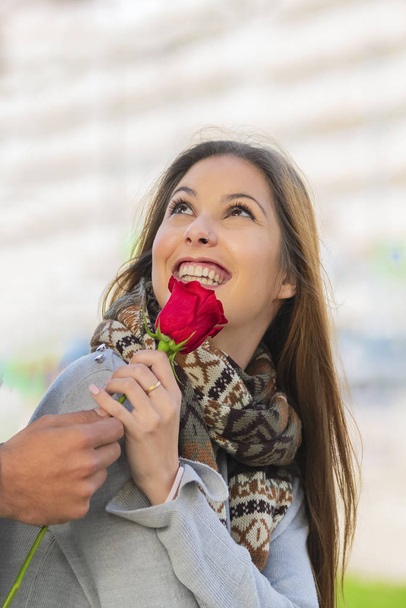 Νεαρή γυναίκα κοιτάζει ψηλά λαμβάνοντας ένα τριαντάφυλλο - Φωτογραφία, εικόνα