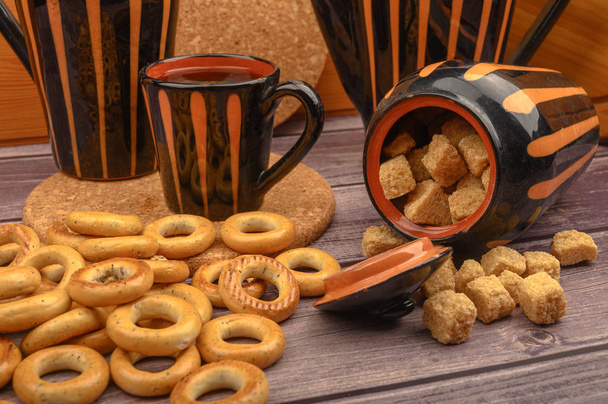 Małe bajgle, brązowy cukier, kubek herbaty i ceramiczne naczynia na drewnianym tle zbliżenie. - Zdjęcie, obraz