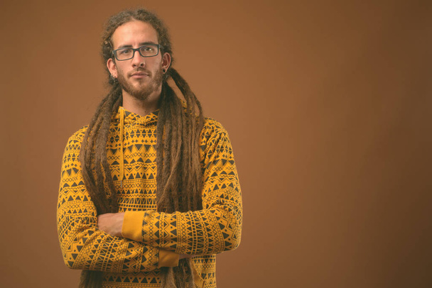 Young handsome Hispanic man with dreadlocks against brown background - Photo, Image
