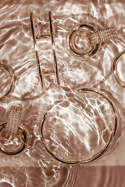 Goldene Armbänder, Ohrringe, Ringe, Schmuck auf goldenem Wasserrücken - Foto, Bild