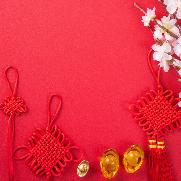 Concept de conception du Nouvel An lunaire chinois - Beau noeud chinois avec fleur de prunier isolé sur fond rouge, pose plate, vue de dessus, disposition aérienne
. - Photo, image