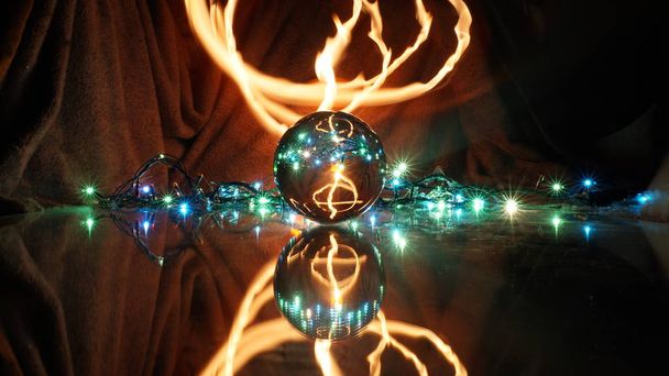 une boule de cristal repose sur un miroir dans lequel se reflètent une guirlande et une flamme de bougie
 - Photo, image