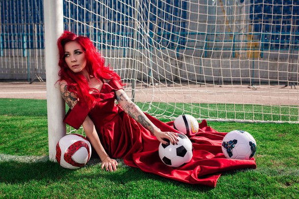 Luxurious woman with red hair and in a red dress plays on the fo - Photo, Image
