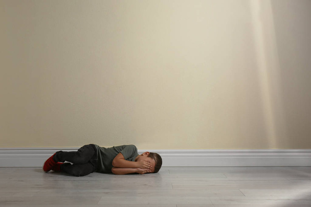 Little boy closing face with hands lying on floor near yellow wall, space for text. Child in danger - Foto, immagini