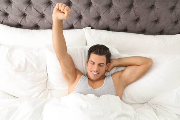 Man awakening in bed at home, top view. Lazy morning - Zdjęcie, obraz