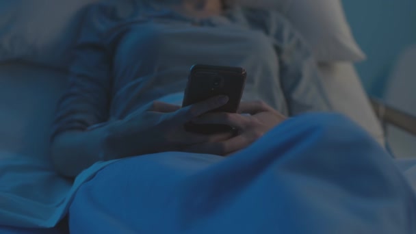 Sad woman in a hospital bed chatting with her phone at night - Video