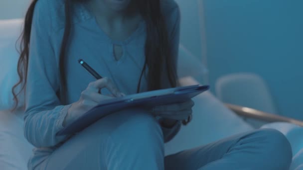 Young patient sitting on a hospital bed and filling in a medical form - Filmmaterial, Video