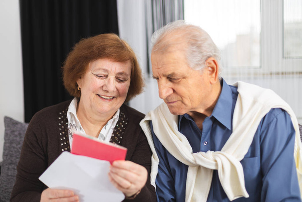 Casal de idosos em pé no sofá e lendo uma carta recebida
 - Foto, Imagem