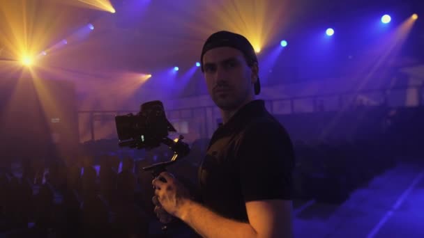 Un hombre joven y atractivo con un estabilizador electrónico de tres ejes y una cámara réflex digital con haces de luz, hace un vídeo cinematográfico
. - Metraje, vídeo
