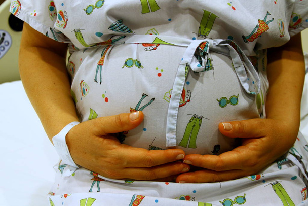 Вид на живіт вагітної жінки з руками
 - Фото, зображення