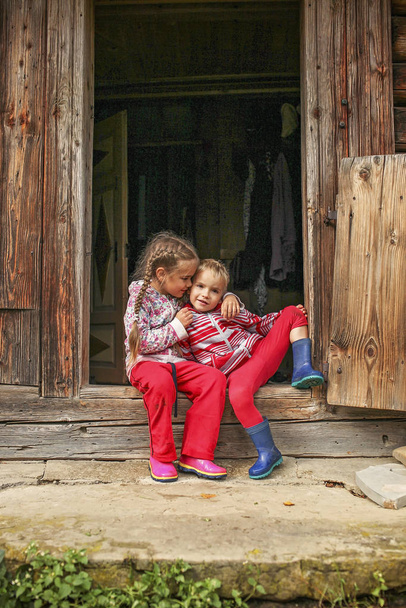Kinder ruhen sich vor der Haustür des alten Holzhauses aus  - Foto, Bild