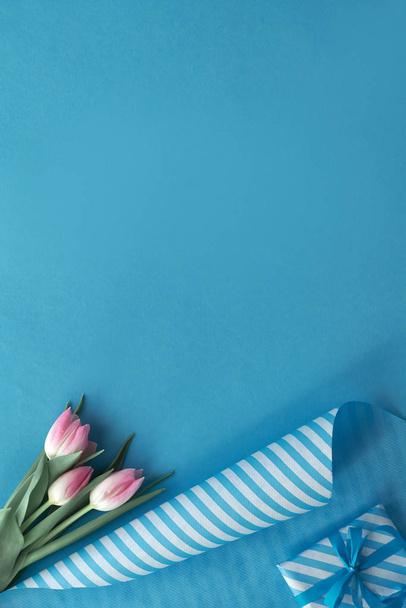 Niebieskie tło z różowymi tulipanami, papier pakowy w paski i prezent - Zdjęcie, obraz
