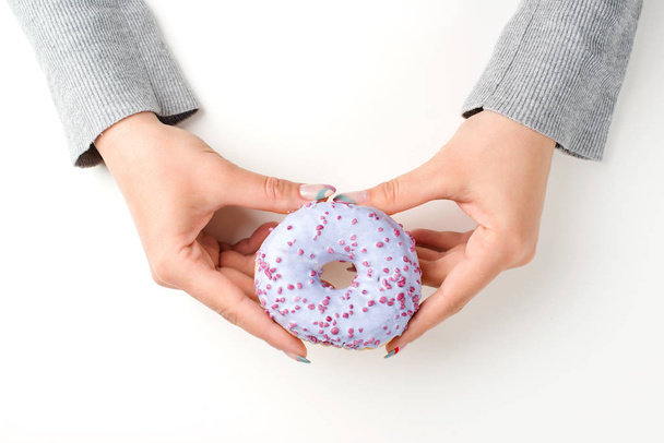 Mãos femininas segurando saboroso donut com polvilhas, vista superior
 - Foto, Imagem