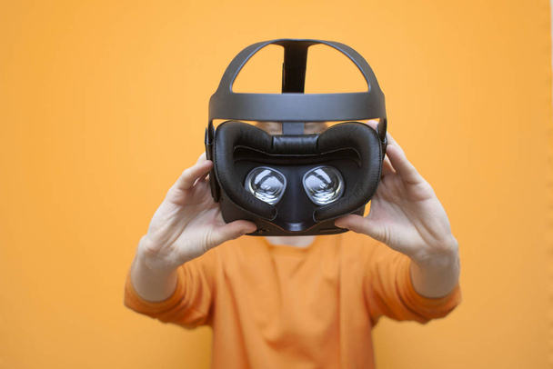 giovane ragazzo tiene occhiali VR su uno sfondo arancione, dispositivo di realtà virtuale
 - Foto, immagini