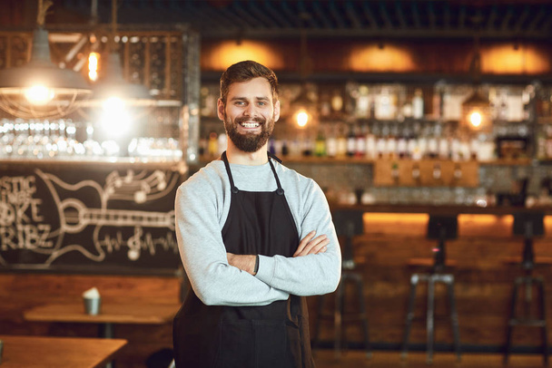 Vousatý usměvavý barman číšník stojí na pozadí baru. - Fotografie, Obrázek