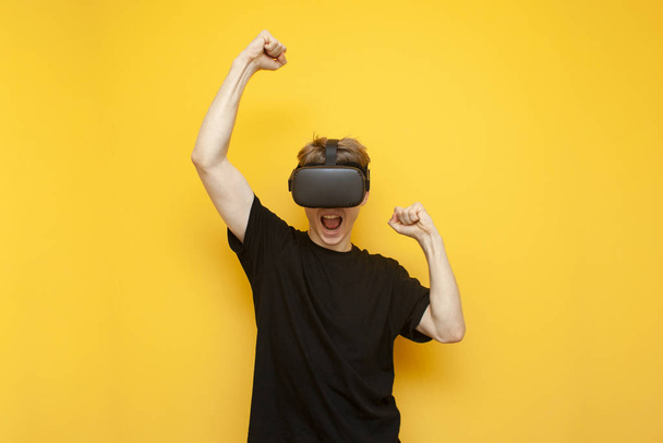 emotional guy with VR glasses wins a virtual game, a gamer rejoices victory over a yellow background - Fotoğraf, Görsel