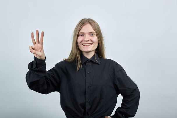 Cheerful young woman showing three fingers, smiling, looking at camera. - Фото, изображение