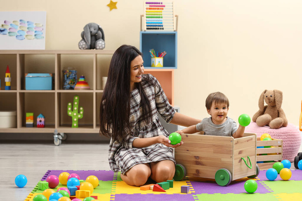Young nanny and cute little baby playing with toys at home - Foto, imagen