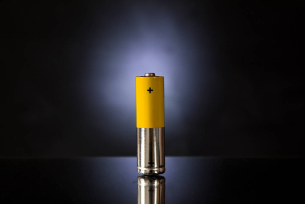 Uma bateria amarelo-prata com um fundo preto retroiluminado
. - Foto, Imagem