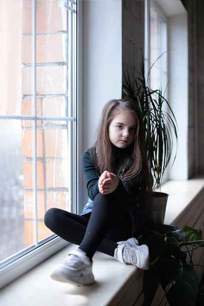 молодая добрая игривая девочка восьми лет с длинными волосами в черной черепахе и джинсах с надписью "ДА"
" - Фото, изображение